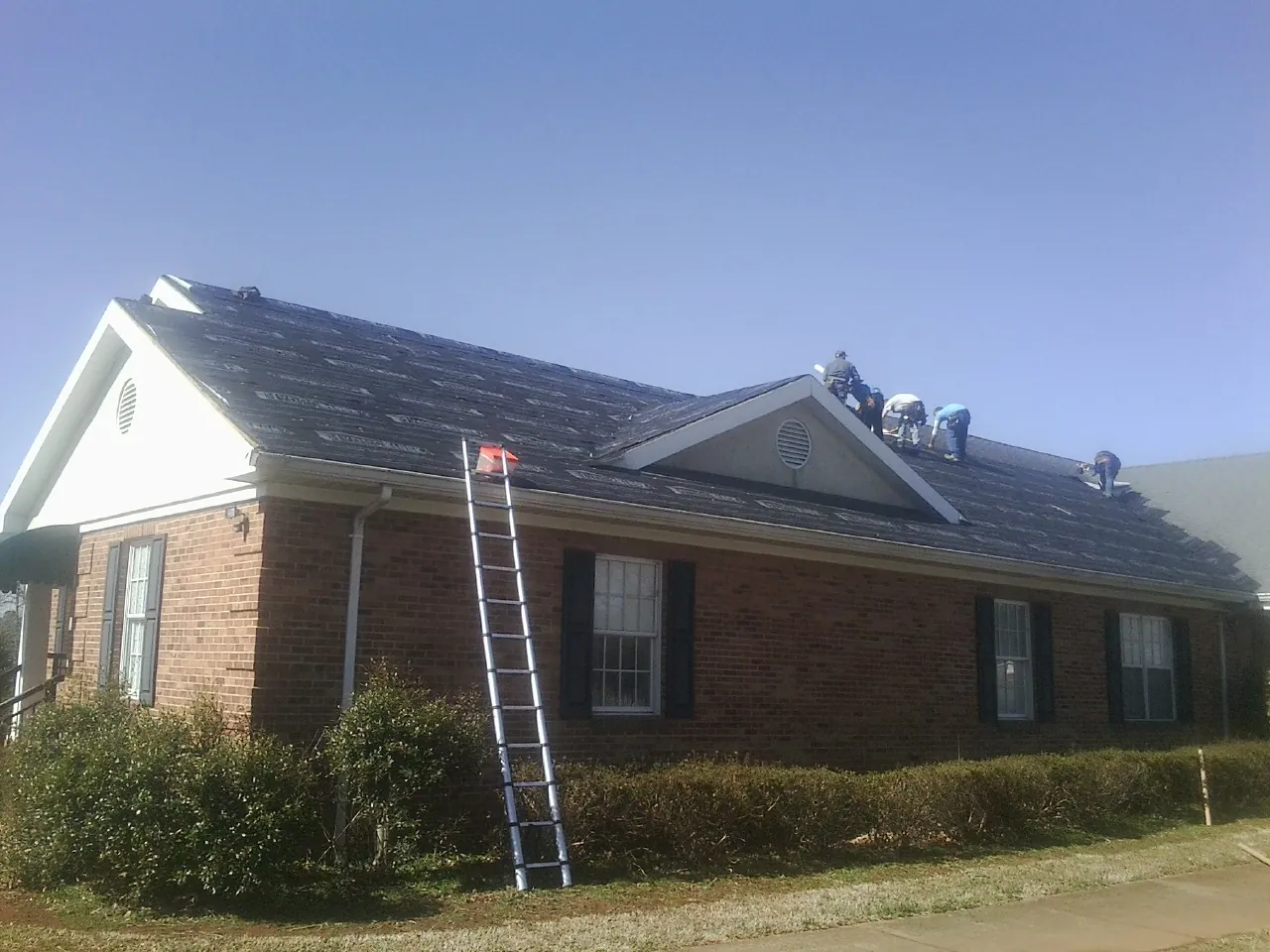 Crew tearing shingles off a brick ranch roof with a ladder set — Metal Roof Repair work by our crew in Dawson