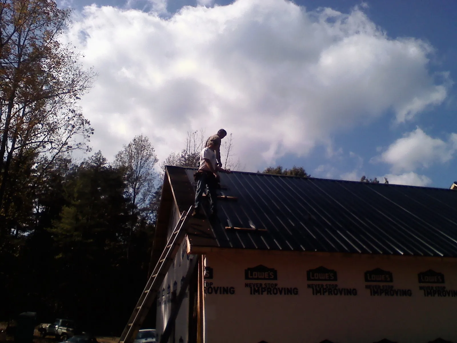 Roofer fastening dark metal panels high against a cloudy sky, from a Roof Inspection job in Dawson